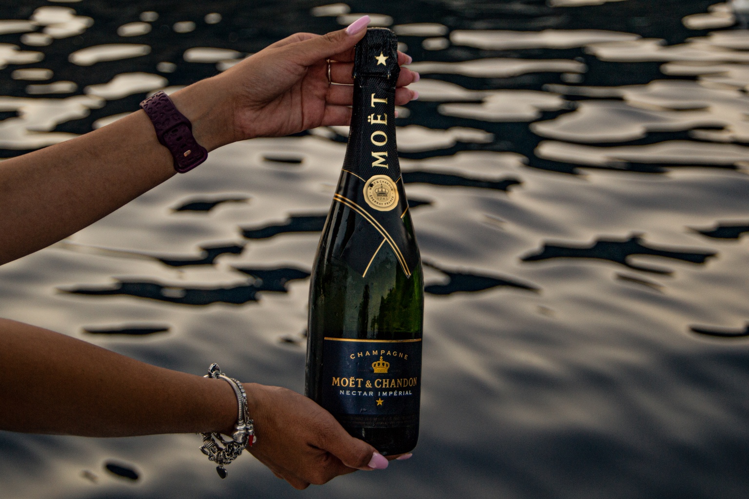 A bottle of Moët & Chandon Nectar Impérial Champagne held above the sea