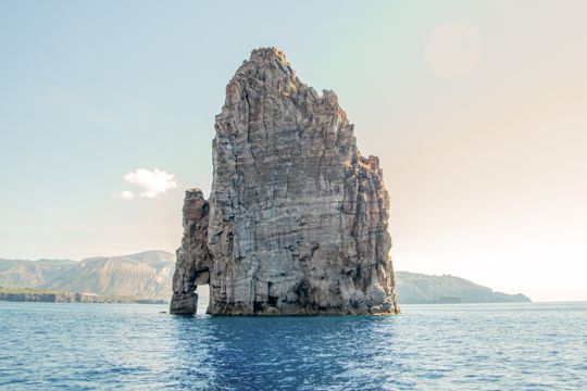 A tall sea stack rising from calm blue water