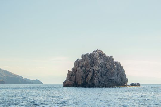A broad sea stack with distant islands behind it